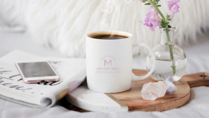 Steaming coffee in a white Mentor Mira mug beside flowers, crystals and a phone